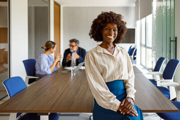 Portrait of confident female professional leaning at conference table with colleagues discussing in the background