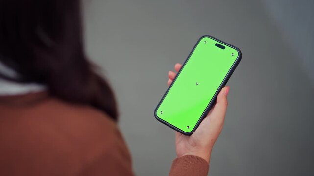 Over the shoulder view of a woman holding a smartphone with a green screen and tracking markers for app mockup, Female is Standing on a Street and Checking Content on a Mobile Device