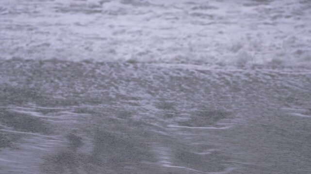 Waves crash at a black sand beach in Vik during changing water patterns