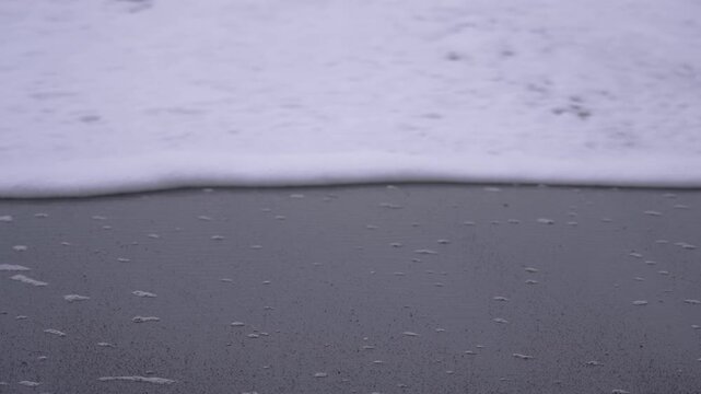 Waves of white foam reach black sand beach at Vik, Iceland at dusk