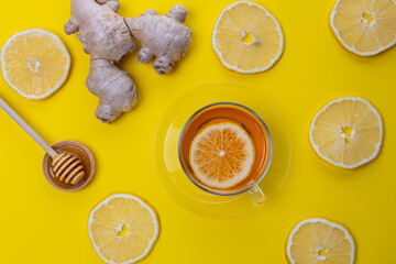 Cup of warm tea with lemon slices and ginger pieces on bright yellow table