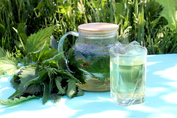 A decoction of nettle leaves in a teapot stands on a wooden table.	