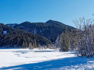 Der Spitzingsee in winter - Snowy landscape, the village, small houses, chalets and hotels along the shore of the frozen lake with views of the forested hills of Rauhkopf and Traubenstein
