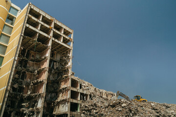 Collapsed building with an excavator clearing heavy rubble at a dusty demolition site in an urban...