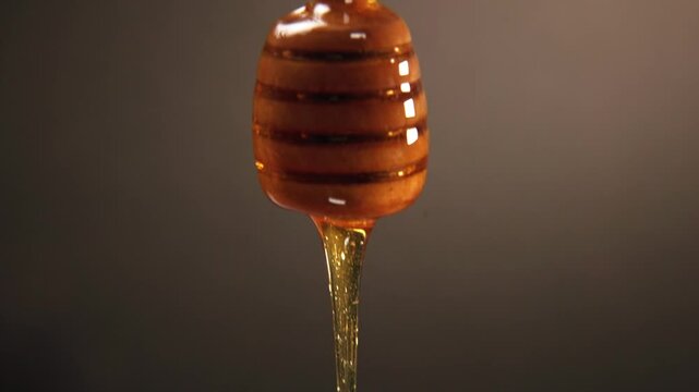 Slow motion slo mo of raw honey bee syrup from beehive with glowing yellow texture falling on top of honeycomb comb with wooden stick and droplets fall slowly for food preparation of sweet treat