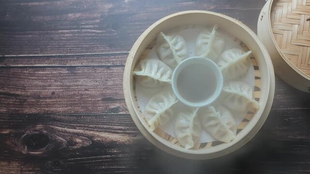 Steaming dumplings served in a bamboo steamer with soy sauce on wooden background.