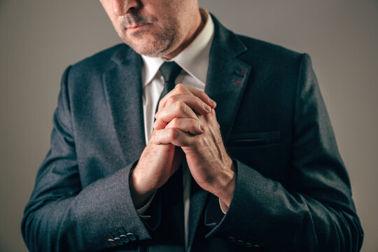 Businessman in suit with clasped hands in prayer or desperation plea