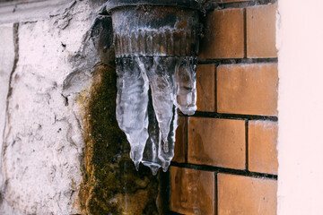 Melting icicles hanging from rusty rain gutter on brick wall in winter