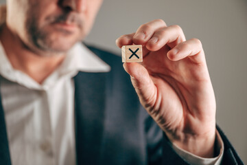 Fototapeta premium Businessman holding wooden block with black X mark for rejection, wrong choice and failure in business.