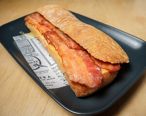 Delicious bacon sandwich served on professional food safe greaseproof paper with newspaper design