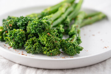 Minimalist food photography of fresh green broccolini served on a white plate on a linen tablecloth