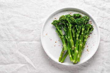 Minimalist food photography of fresh green broccolini served on a white plate on a linen tablecloth