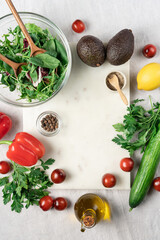 Fresh Lettuce Leaves in Glass Bowl, Marble Cutting Board and Salad Ingredients on Linen Kitchen Table, Top View