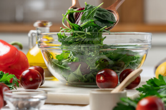 Fresh Lettuce Leaves in Glass Bowl on Kitchen Table Surrounded by Salad Ingredients and Vegetables. Healthy Diet Food Concept