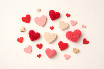 Fototapeta premium A bunch of hearts are scattered around a white background. The hearts are of different sizes and colors, with some being red and others pink. Scene is one of love and affection