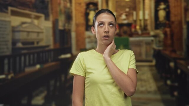 Woman with hand on neck and pensive face in church building, yellow shirt and wooden pews visible; uncertainty discomfort.
