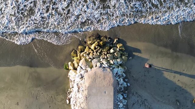 Top view of person enjoying the beach with ocean waves and sand split, Cinematic zenith view of person relaxing on the beach sand with blue waves. High quality 4k footage