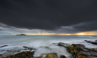 Fototapeta premium A stormy ocean with a rocky shoreline. The sky is dark and cloudy, and the water is choppy