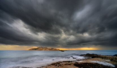 A stormy ocean with a rocky shoreline. The sky is dark and cloudy, and the water is choppy