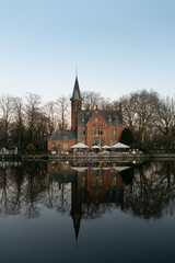 Neo-gothic lakeside castle restaurant reflected in still water at blue hour in Bruges, Belgium, vertical winter travel cityscape