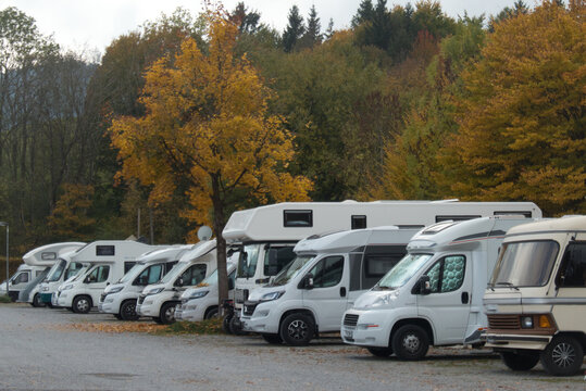 Mehrere Wohnmobile stehen nebeneinander auf einem Parkplatz vor herbstlich gef&auml;rbten B&auml;umen