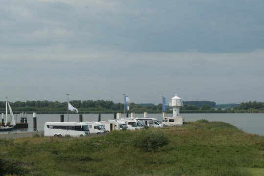 Mehrere Wohnmobile stehen an der Hafeneinfahrt von Gl&uuml;ckstadt an der Elbe neben einem Leuchtturm, umgeben von Wiesen und Wasser
