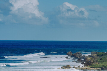 Waves breaking along a rocky coastline with deep blue ocean and soft clouds above the horizon, creating a natural coastal seascape
