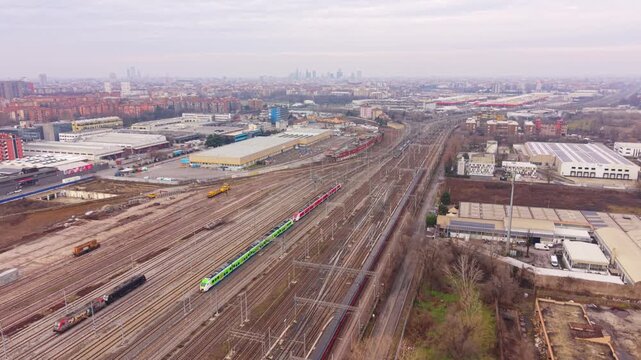 An expansive railway yard stretches out beneath a cloudy sky, showcasing a network of tracks leading towards an urban skyline, a testament to industry and transport.