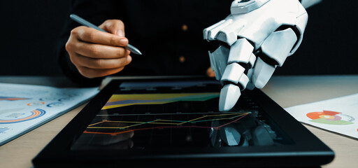 A captivating scene of a robotic arm and a human hand working together on a touchscreen device, demonstrating advanced technology in data analysis and visualization.Noogenesis