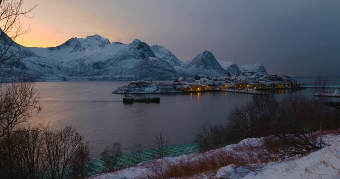 Hus&oslash;y im Winter zur blauen Stunde, Fischerboot f&auml;hrt in den Hafen ein, schneebedeckte H&auml;user und ruhiger Fjord unter kaltem Abendlicht in einer nordnorwegischen K&uuml;stensiedlung