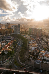 Fototapeta premium Aerial cityscape in Las Palmas de Gran Canaria shows S curve multilane roads, high rises, terraced blocks, winter sun rays, mountains, and traffic with pedestrians moving.