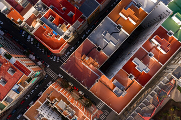 Aerial overhead view of Las Palmas de Gran Canaria city block. Grid streets, colorful flat rooftops in red, orange, white, long afternoon shadows, crosswalks, parked cars, STOP marking.