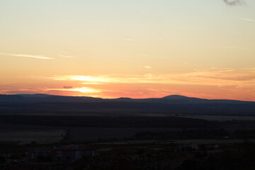 Sunset over rolling hills with vibrant orange and pink hues illuminating the sky and silhouetting...