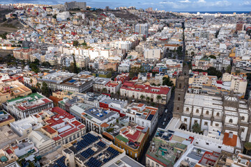 Fototapeta premium Aerial view of Vegueta in Las Palmas de Gran Canaria shows the Cathedral of Santa Ana, narrow streets, pastel rooftops with solar panels, hills, and the Atlantic horizon.