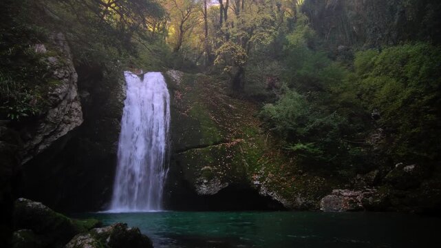 Secret canyon harboring radiant waterfall cascading into soothing azure waters amidst lush greenery, Hidden gorge with shimmering cascade flowing into tranquil sapphire pool amid vibrant green foliage