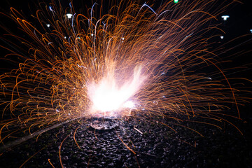 Sparks flying from ground level explosion at night.