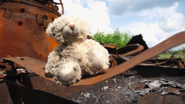 Dirty teddy bear sits on rusted destroyed tank. The fragile toy on the remains of a war machine becomes a painful symbol of lost childhood echoing the devastation and sorrow in Ukraine. Close up