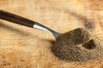 Freshly ground black pepper in a wooden spoon on rustic cutting board.