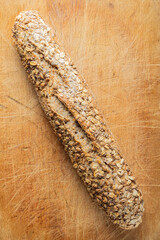 Rustic multigrain baguette with oat seeds on wooden cutting board.