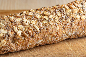 Rustic multigrain baguette topped with mixed seeds on wooden surface.