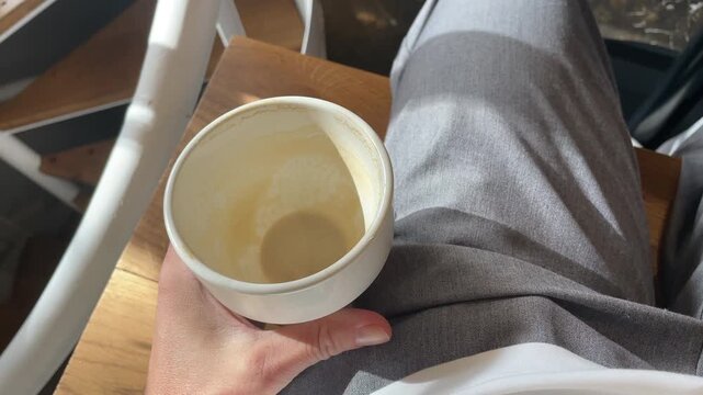 POV hand holding a small cup with leftover coffee at the cafe