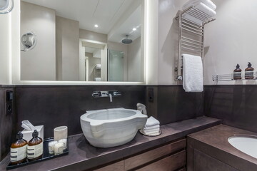 A stylish bathroom setup shows a bowl sink, mirrors, and storage areas. There are toiletries on display and towels hanging. The space is well-lit and organized.