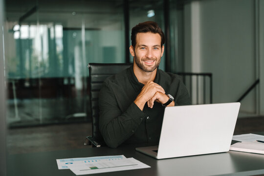 Happy portrait young European business man ceo trader using laptop computer, working in office workplace. 30s middle-aged Hispanic smiling handsome businessman entrepreneur student looking at camera