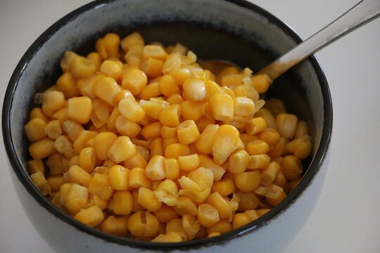 Close-up of a small colored porcelain bowl with fresh yellow corn and a spoon on the table