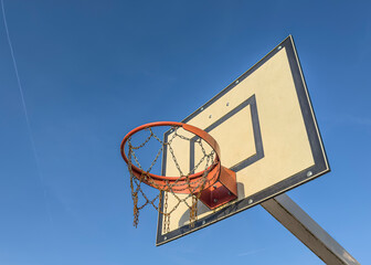 Naklejka premium Close-up of a weathered basketball backboard and orange rim with a chain-link net.