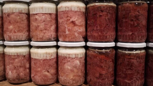 Close rows of traditional meat preserves in glass jars show layered textures and natural colors creating an authentic rustic food atmosphere highlighting handcrafted preparation and regional culinary 