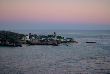 Tranquil coastal view of the Dominican Republic at dusk with soft pastel sky and calm ocean water, viewed from an elevated perspective.
