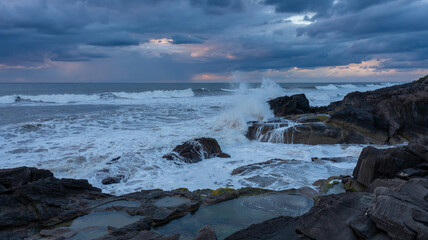 Waves crash on rocks under a cloudy sky