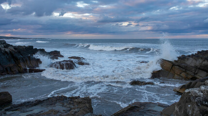 Waves crash on rocks undera cloudy sky