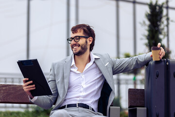 Young businessman sitting on a bench outdoors, carefully reviewing a paper report.